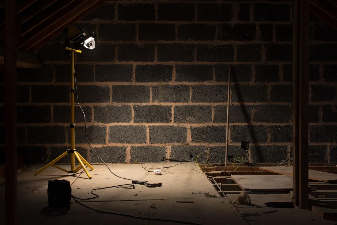 Grenier en préparation avant la pose de l'isolant, éclairé par une lampe de chantier (Bavent, Calvados)